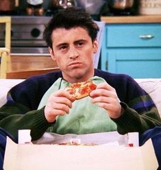 a man sitting on a couch eating a slice of pizza