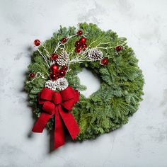 a green wreath with red bows and pine cones