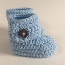 a blue crocheted boot with a button on the front and side, sitting on a white surface