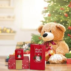 a brown teddy bear sitting next to christmas presents on the floor with a tree in the background