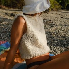 a woman sitting on the beach wearing a white hat