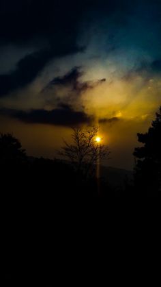 the sun is setting behind some trees in the dark night sky with clouds above it