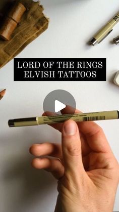 the lord of the rings elvish tattoos is holding a pen in front of some other items