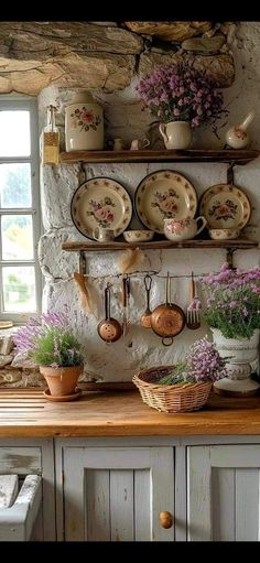 an old fashioned kitchen with pots and pans on the wall, flowers in vases