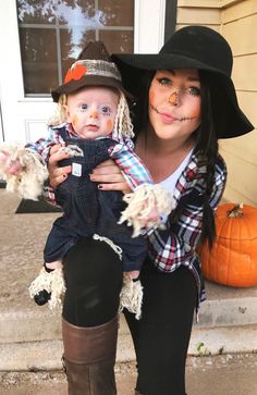 a woman holding a baby wearing a witch costume and hat on her head while standing in front of a house