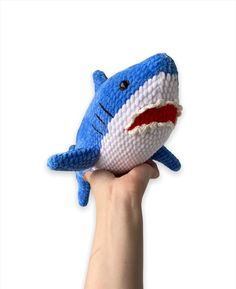 a hand holding a stuffed toy that looks like a shark