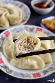 some dumplings are being held up by chopsticks with sauce on the side