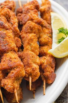 chicken skewers with lemon wedges and parsley garnish on a white plate