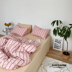 a bed with pink and white striped sheets on it next to a potted plant