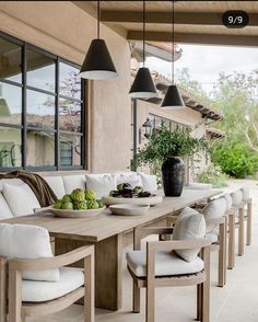 an outdoor dining area with white cushions and wooden table surrounded by chairs, potted plants and large windows