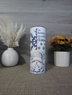 a white vase sitting next to two flowers and a clock on a table with snowflakes