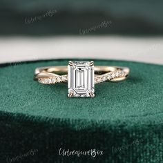 an emerald colored diamond engagement ring sits on top of a green velvet box