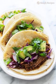 three pulled pork tacos on a plate with lettuce and avocado