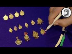 a person is holding a pen and some gold jewelry on a purple surface with a coin in the background