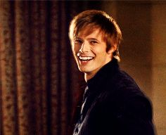 a young man smiles while standing in front of curtains