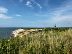 a light house sitting on top of a lush green hillside next to the ocean with tall grass