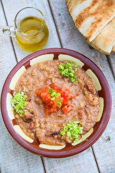 a bowl filled with food next to bread on top of a wooden table and a glass of olive oil