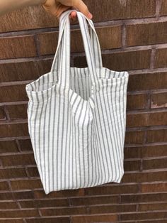 a person holding a white and black striped bag in front of a brick wall,