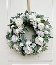 a wreath with white flowers and greenery hangs on a door