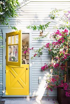 a yellow door and some pink flowers on the side of a house