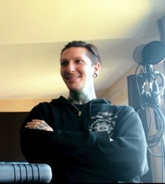 a man with his arms crossed standing in front of a microphone and recording equipment behind him