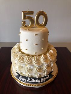 a 50th birthday cake with white frosting and gold decorations on top, sitting on a wooden table