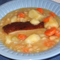 a bowl of food with meat, potatoes and carrots on the side is sitting on a blue table cloth