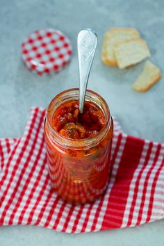 a spoon in a jar filled with food on top of a red and white checkered napkin