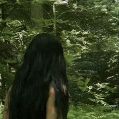 a woman with long black hair standing in the woods