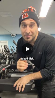 a man in a black shirt is sitting on a treadmill and has his thumb up to the camera