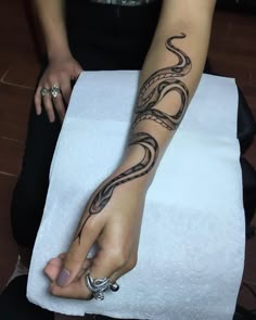 a woman with a snake tattoo on her arm and hand is sitting on a towel