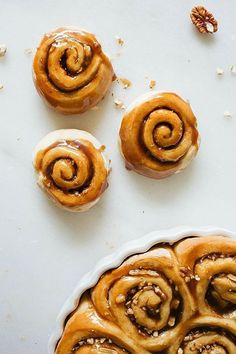 some cinnamon rolls are sitting on a white surface next to other pastries and nuts