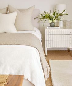 a bed with white linens and pillows in a small room next to a dresser