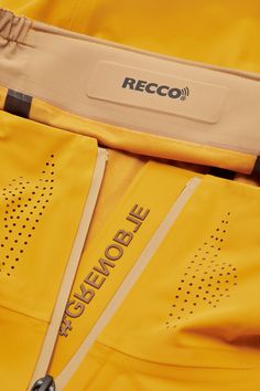 the back end of a yellow jacket with black lettering on it and zippers at the bottom