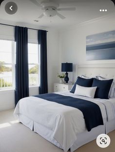 a bedroom with blue and white bedding, two windows, and a painting on the wall