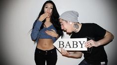 an older man and young woman posing for a photo with the baby sign in front of them