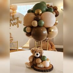 a teddy bear sitting on top of a table with balloons in the shape of trees