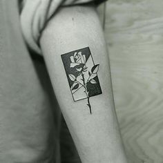 a black and white photo of a rose tattoo on the right arm, with an open square behind it