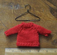 a red knitted sweater sitting on top of a wooden floor next to a ruler