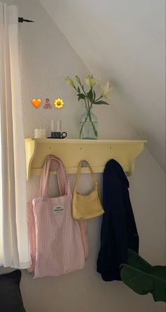 two purses are hanging on the wall next to a vase with flowers in it