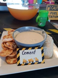 a plate with crackers and dip on it sitting next to a bowl of dip