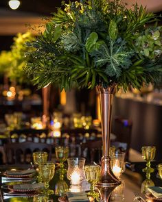 a tall vase filled with greenery sitting on top of a table next to glasses