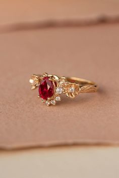 a gold ring with a red stone surrounded by small white diamonds on a piece of paper