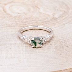 a white gold ring with a green and white stone in the center on top of a piece of wood