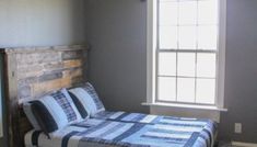 a bed sitting under a window next to a wooden headboard in a room with gray walls