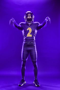 a football player wearing a uniform and holding his hands up in the air while standing on a purple background