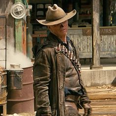 a man wearing a cowboy hat and leather jacket standing in front of an old building