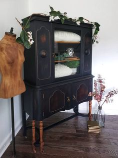 an old black china cabinet with white flowers on it and a mannequin standing next to it