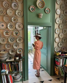 a woman in a dress and hat looking into a room with plates on the wall