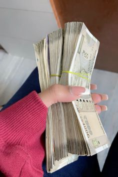 a person holding stacks of money in their hand with pink sweater on and blue leggings